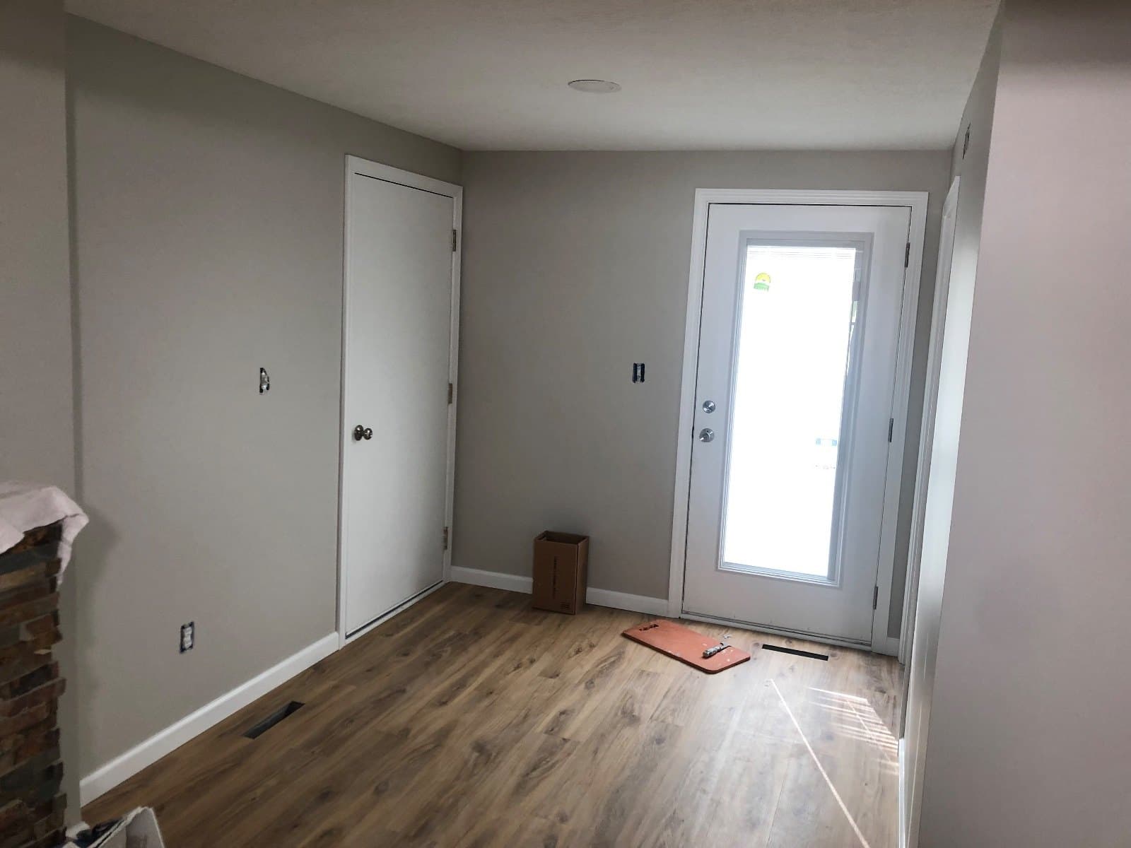 An entry with a glazed door and a closet door, a carton and a mat on newly laid vinyl plank.