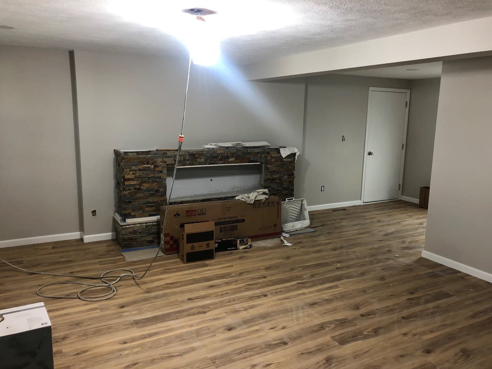 A stone-faced bar under construction with cartons and a coiled cord on a finished vinyl plank floor.
