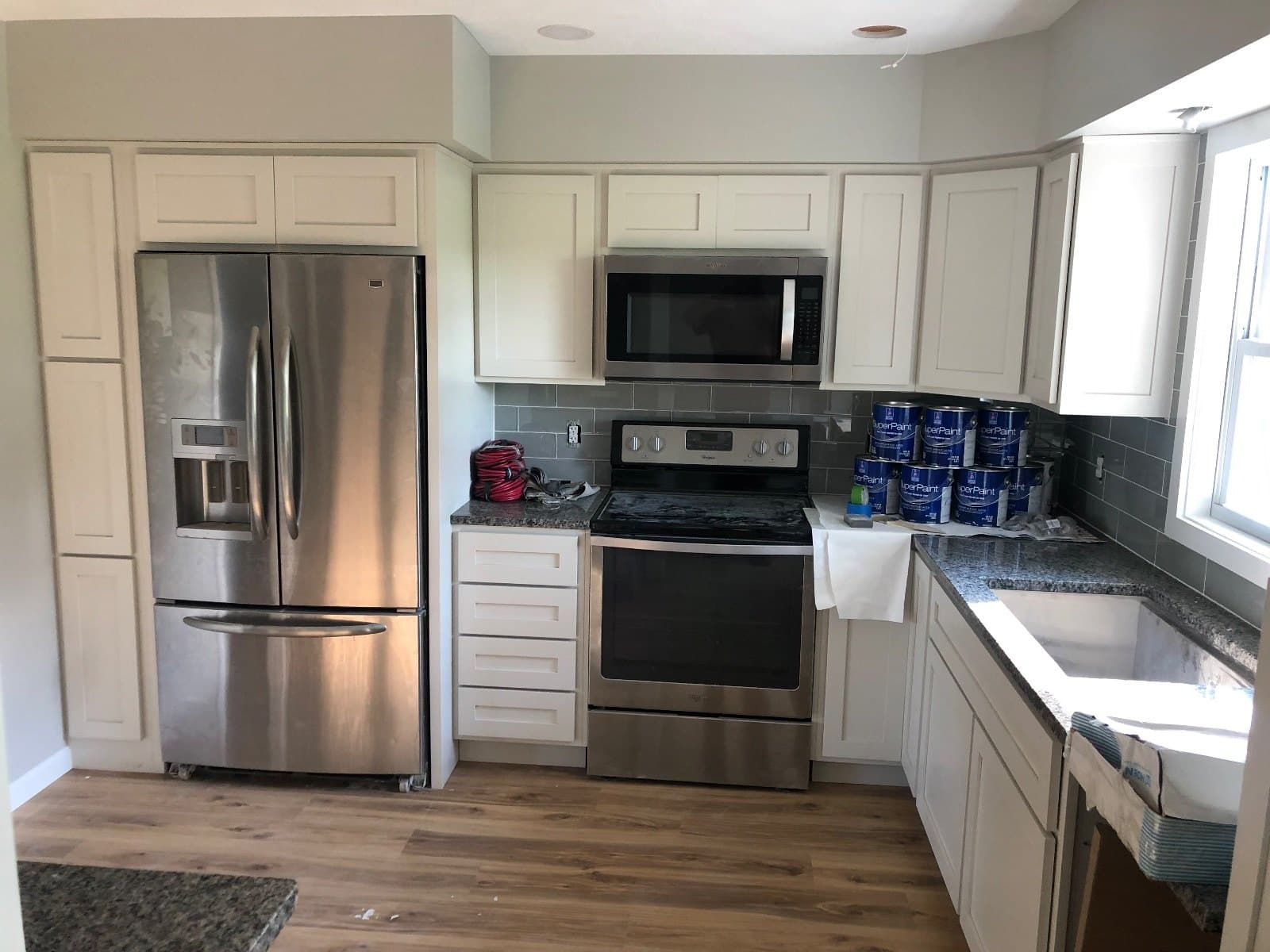 A kitchen with paint pails lined along the counter and protective cloth down, vinyl plank already laid.