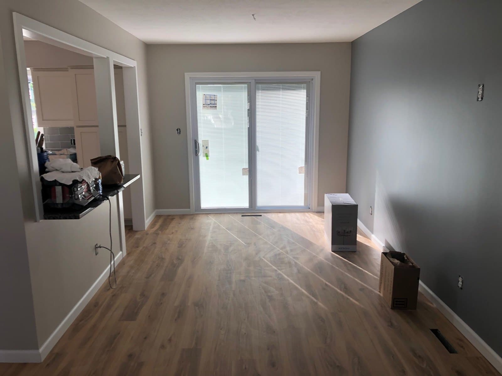 A room with a sliding patio door, a carton and a small unit on the floor, vinyl plank to the threshold.