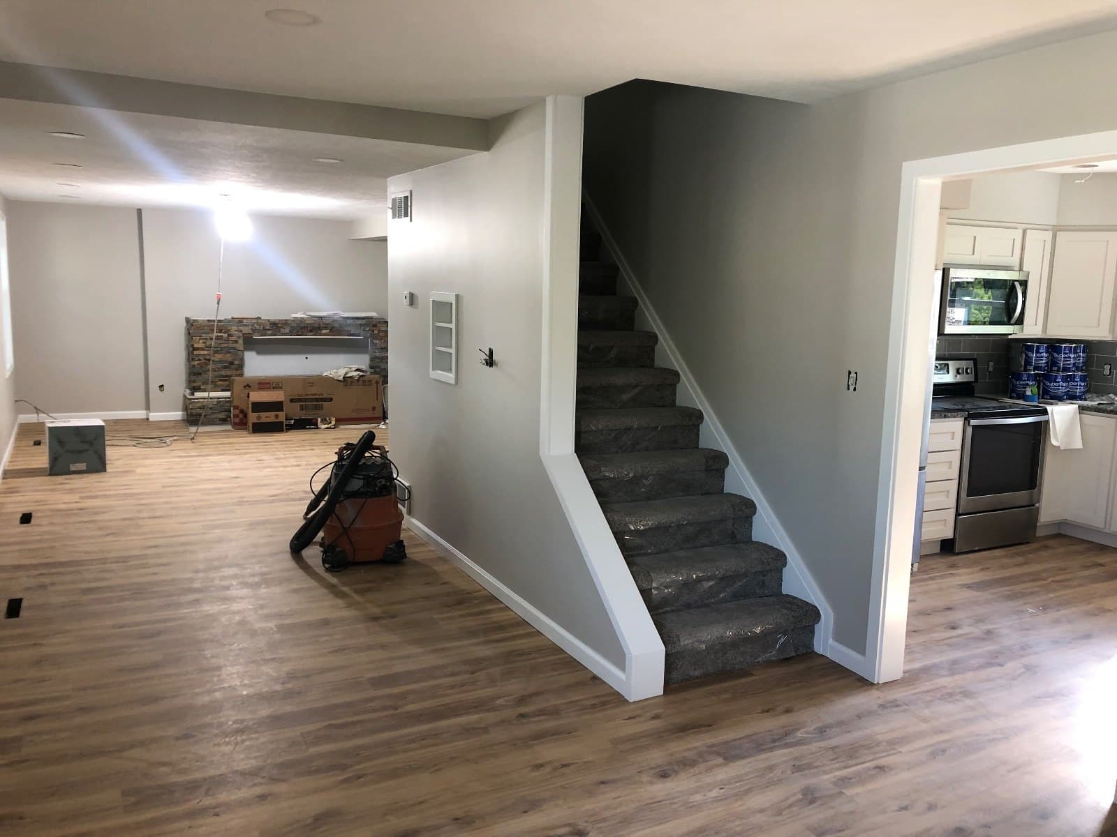 A covered stair rising beside a kitchen doorway, tools at the foot of it on vinyl plank.