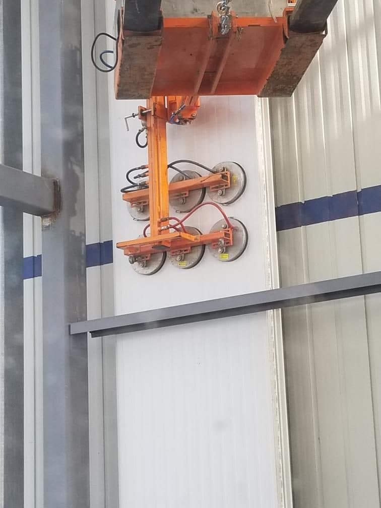 Close view of a vacuum lifter holding an insulated metal panel against the wall line.