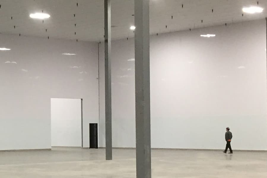 A large empty room lined floor to ceiling in smooth white interlocking panels, a worker walking along the far wall.