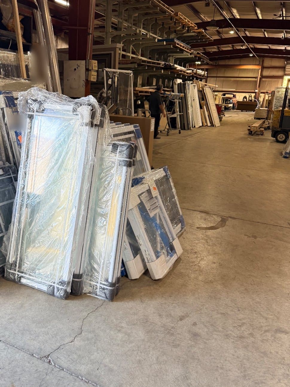 Wrapped white vinyl windows stacked on the floor of the D.W. Ross warehouse on West 63rd Street in Cleveland, the main aisle and steel racking behind them.