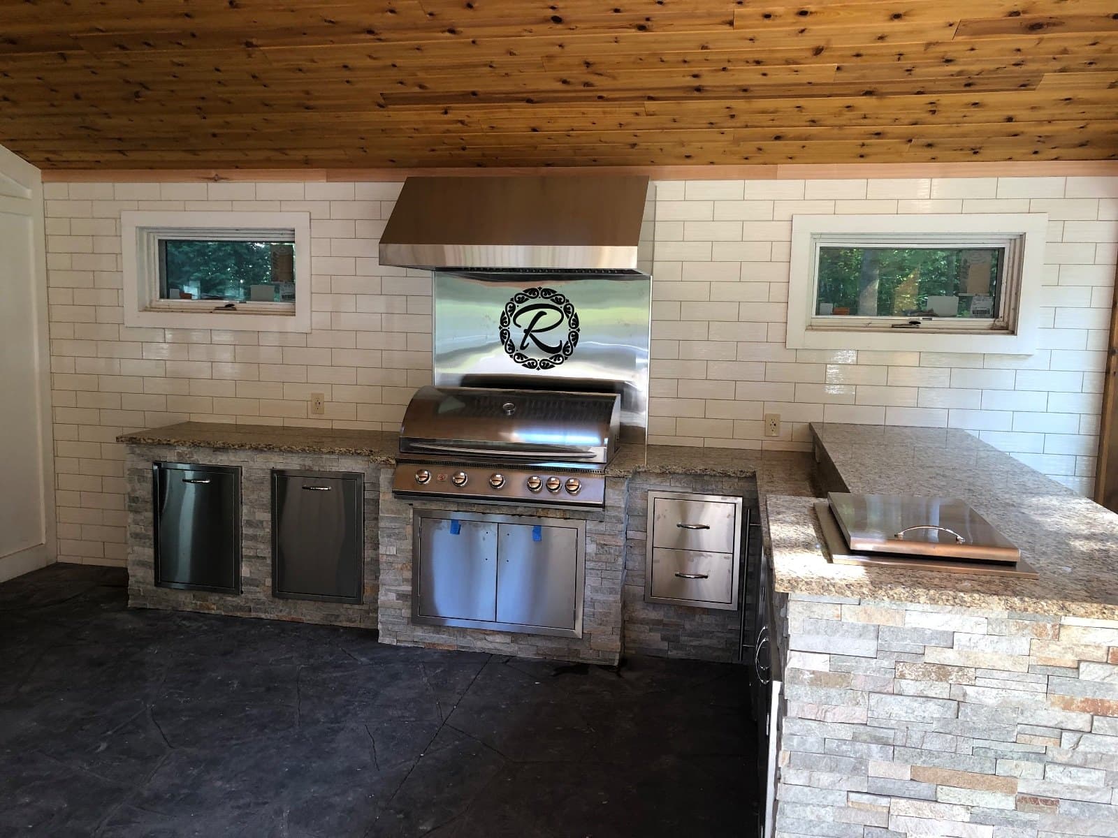 Windows and a serving opening in an outdoor kitchen, stone base and a stainless grill under the counter.