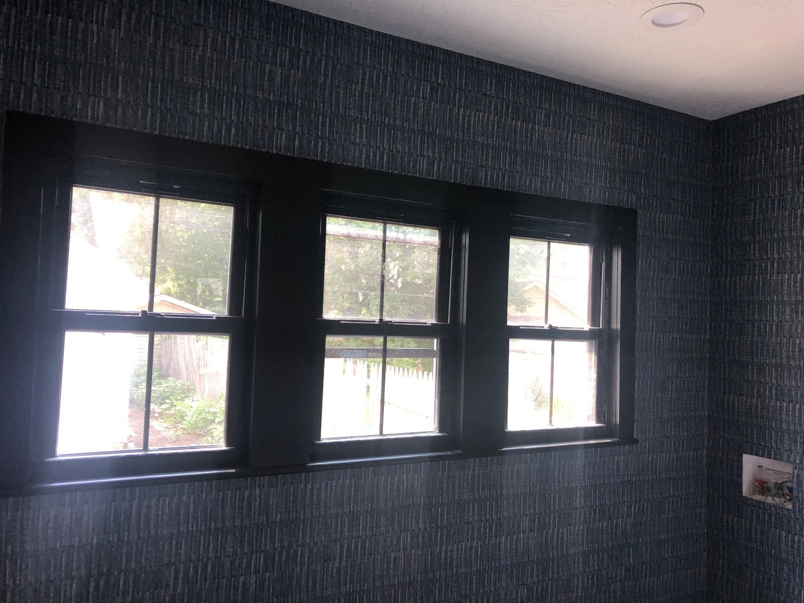 A run of dark-framed windows across a dark brick wall, daylight coming through.