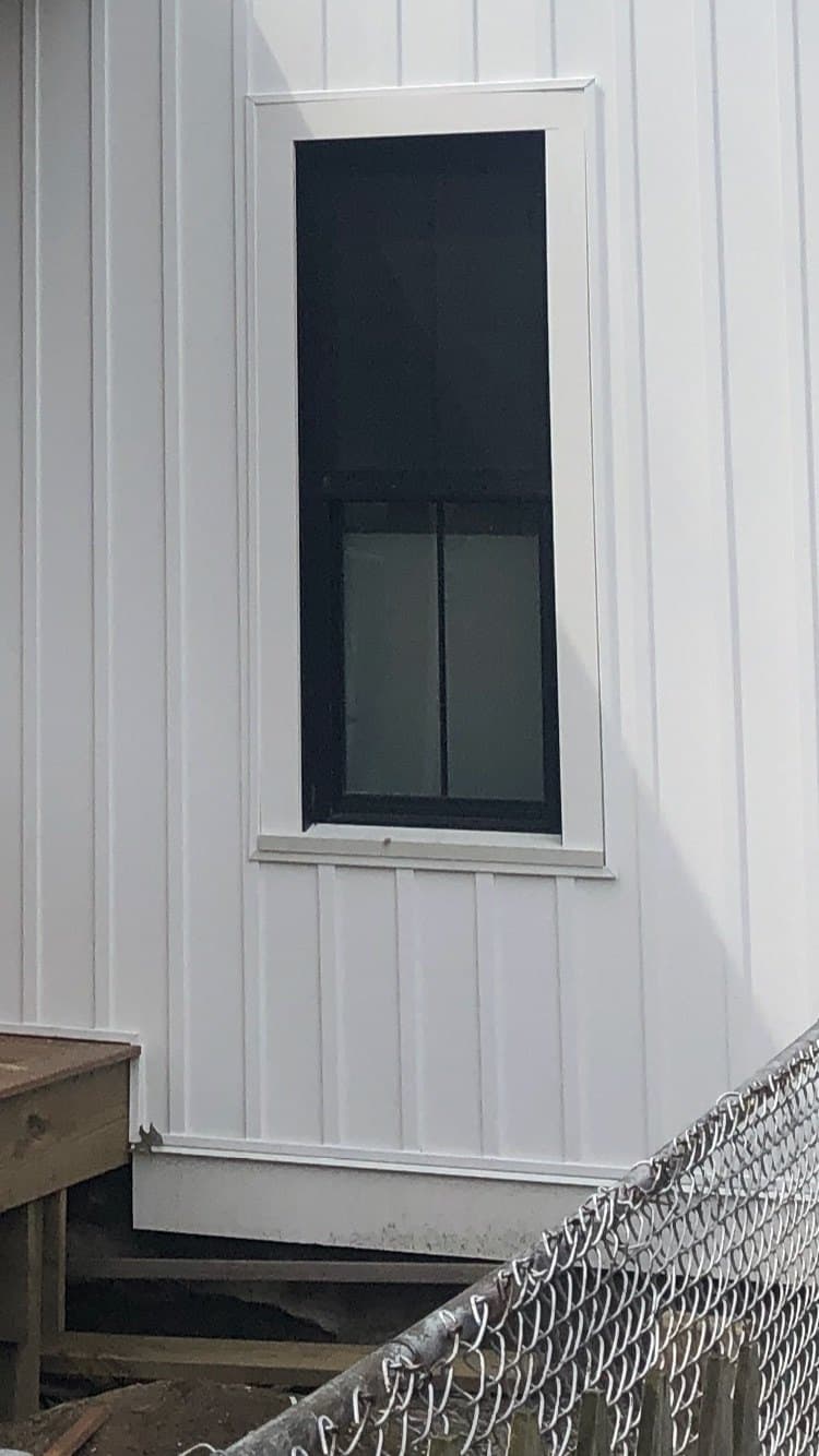 A single tall dark-framed window in white board-and-batten siding.