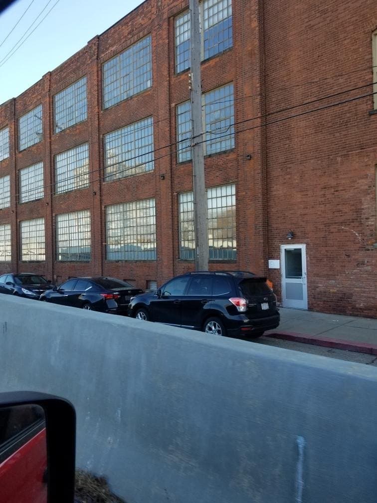 Banks of steel windows across the face of a brick industrial building, cars parked below.