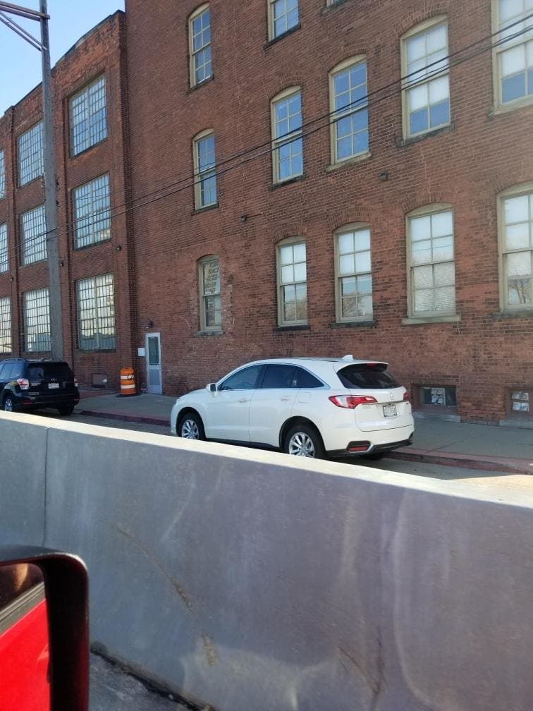 A brick industrial building seen from the street, steel windows across three floors, cars parked below.