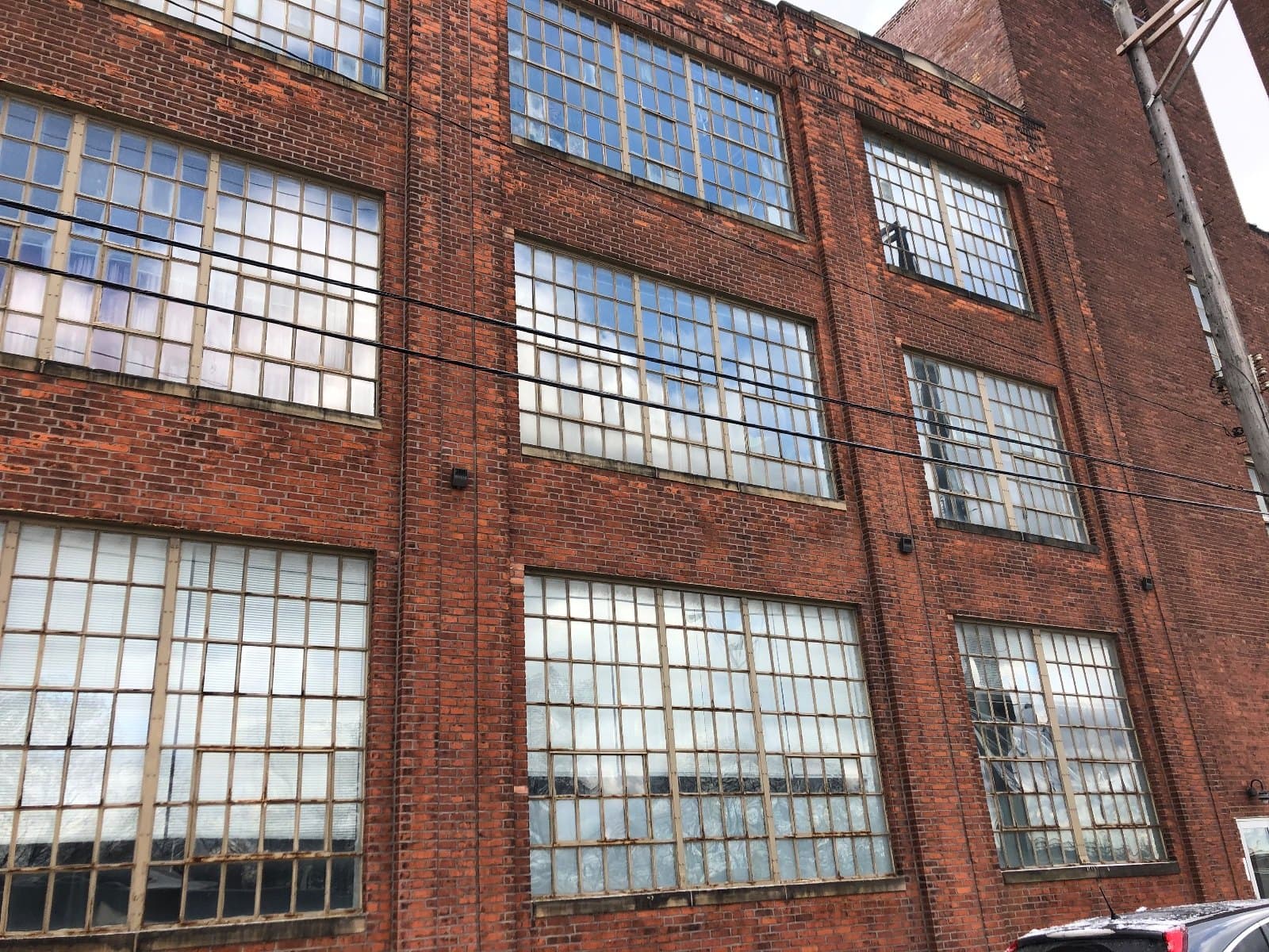 Steel windows in a brick industrial wall, several floors of divided lites seen from close below.