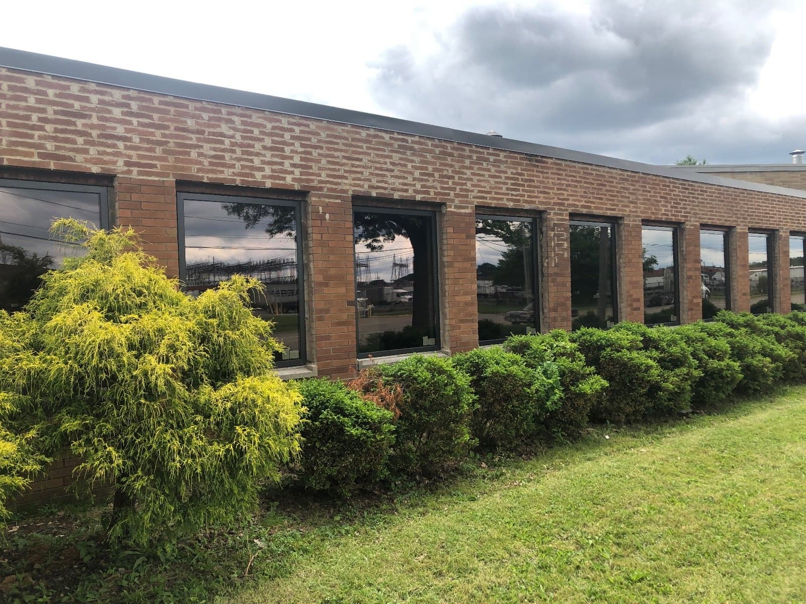 A low brick commercial building with a continuous run of dark windows along the elevation, shrubs in front.