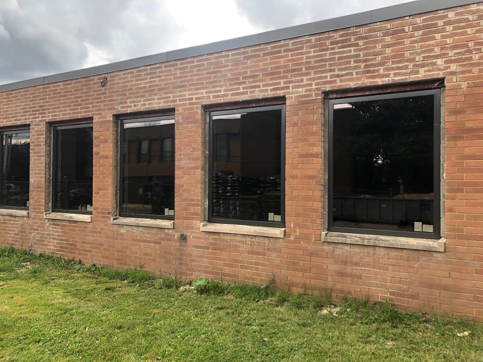 A run of dark windows along a brick commercial building, lawn in the foreground.