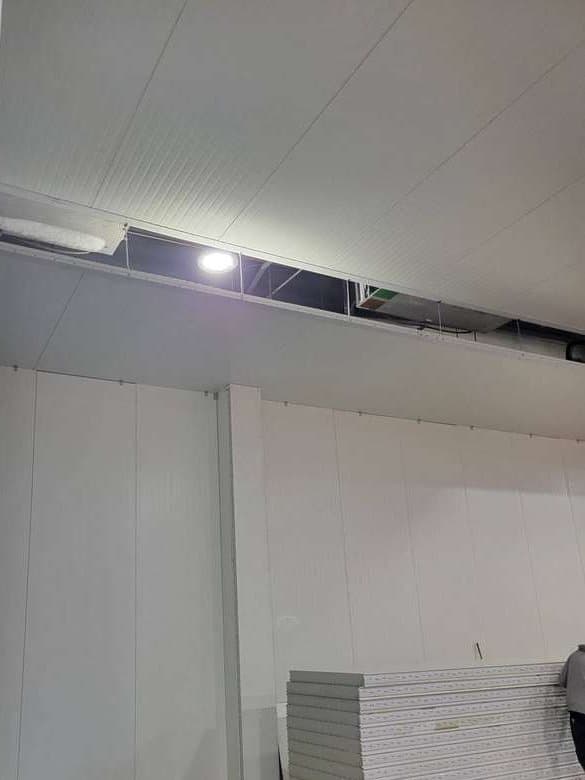 White insulated panel walls and ceiling in place inside a plant, a stack of panels on a cart below.