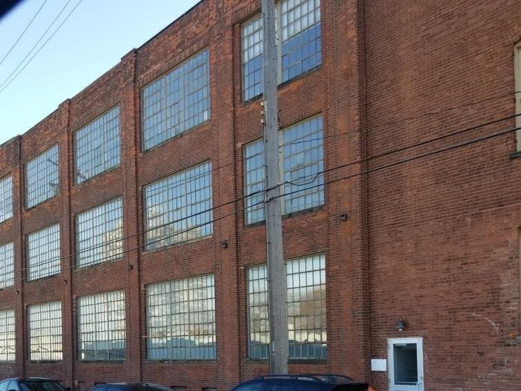 Before: the brick warehouse from the street, original steel windows in light frames across three floors.
