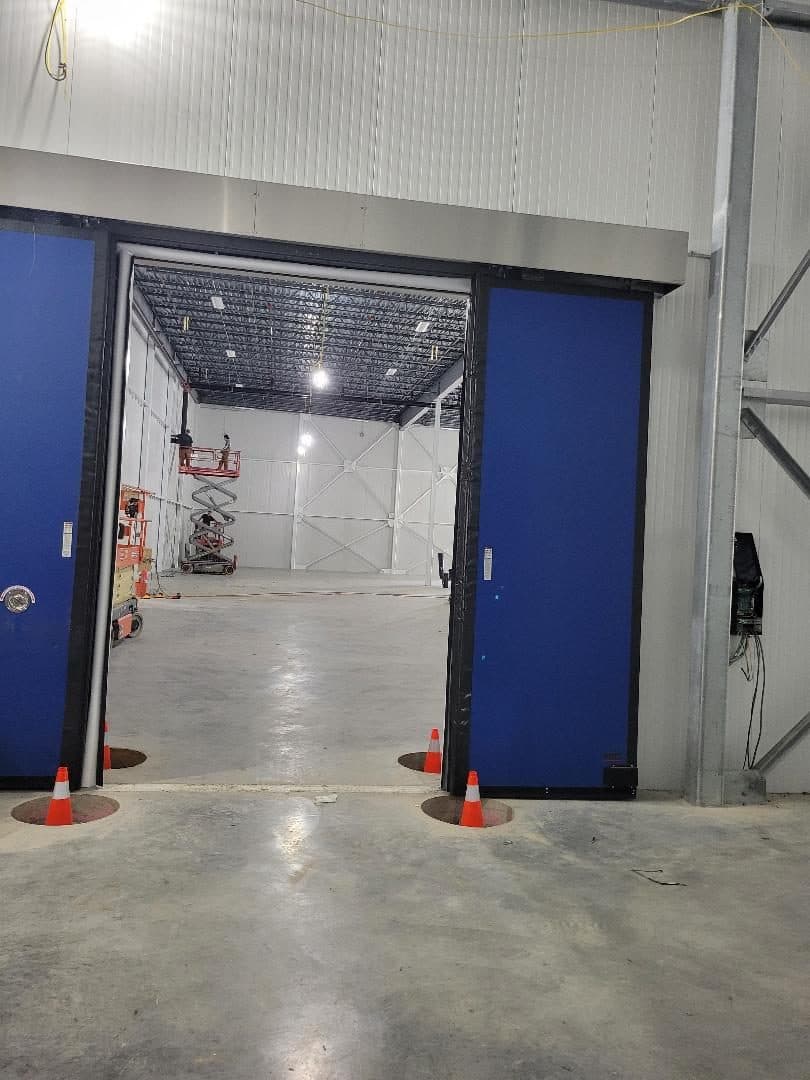 Blue freezer doors set in a white insulated panel wall, open to the freezer beyond.