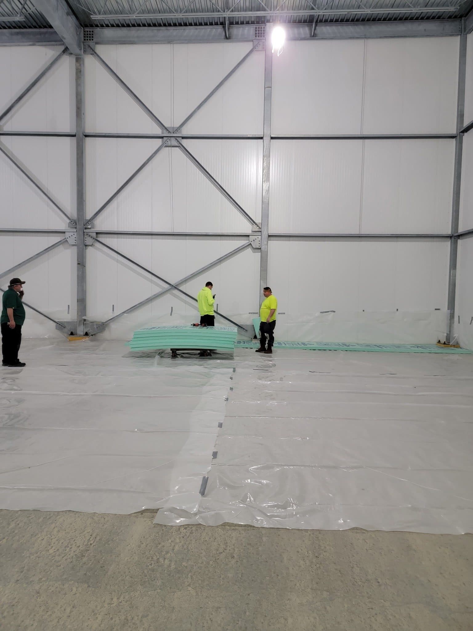 Crew laying a vapor barrier over freezer floor insulation inside the panel envelope.