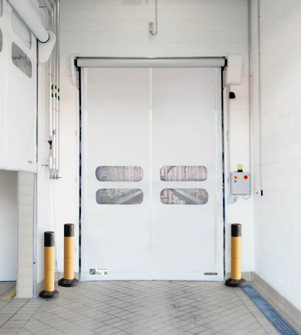 White DynamicRoll Food PE high-speed door with vision panels between yellow bollards