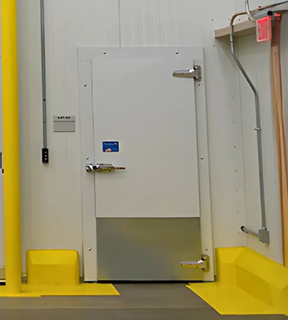 White Jamofoam I swing cooler door with a stainless kick plate and strap hinges between yellow guard posts