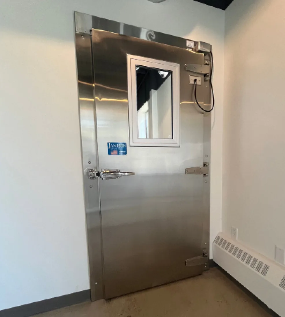 Stainless steel Jamofoam II swing cooler door with a vision window and a power operator above the frame