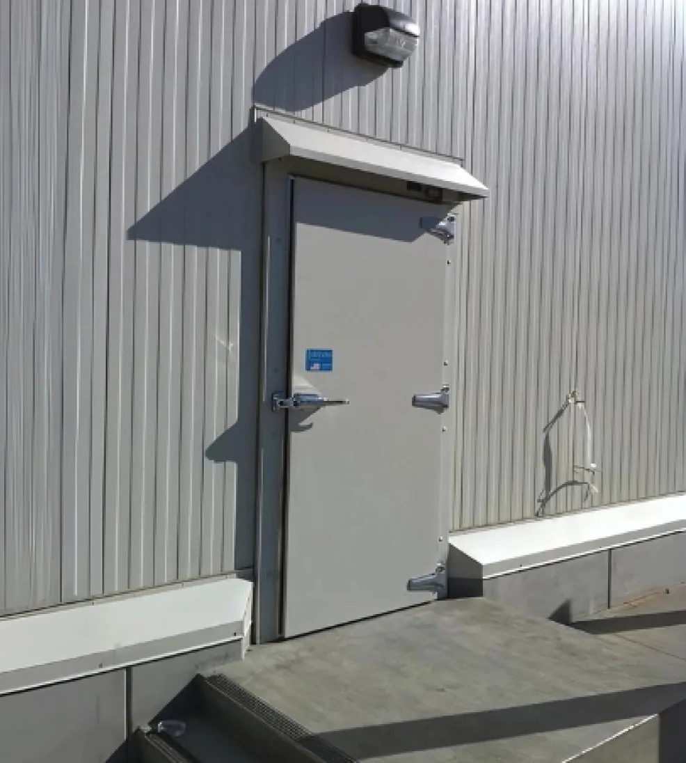 Gray Jamofoam II swing door under a rain hood on an insulated metal exterior wall, at the top of a step