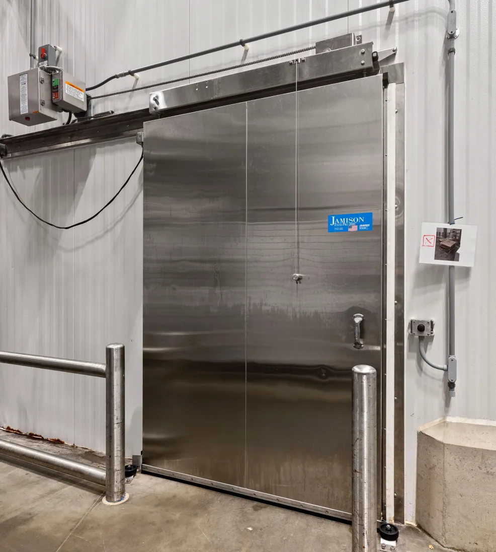 Stainless steel Jamofood sliding cold room door with a power operator between guard rails