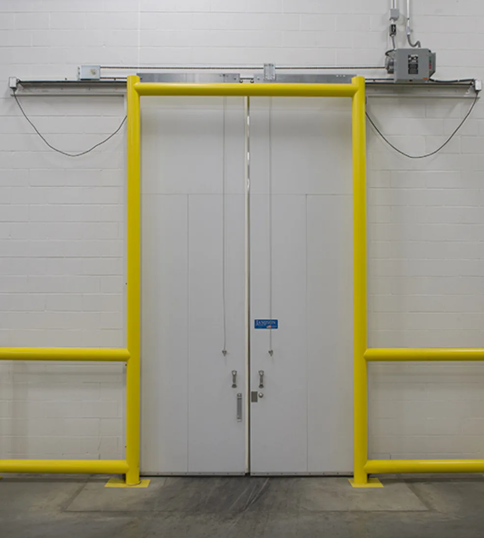 White Jamoglide bi-parting sliding cooler doors with an overhead operator and a yellow guard frame