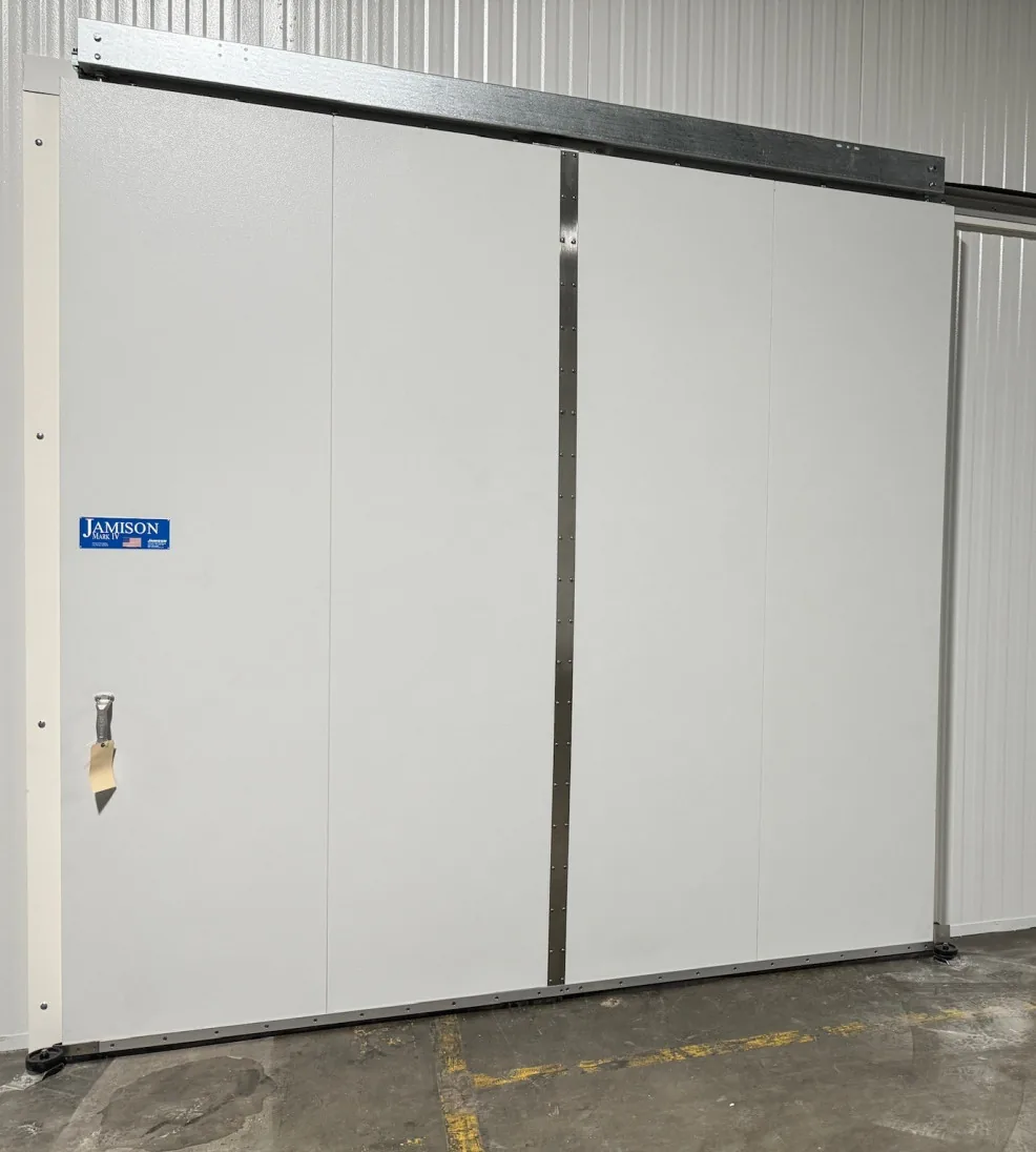 Large white Jamoglide bi-parting sliding cooler door on its overhead track