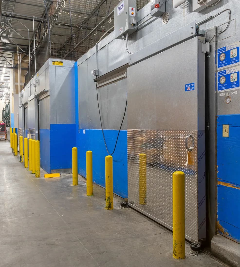 Row of Jamoglide Retail sliding cooler doors along a grocery warehouse aisle with yellow bollards