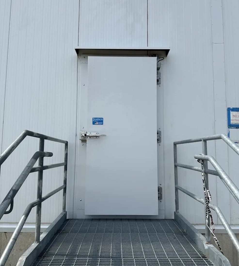 White Jamoguard overlap door at the top of a steel stair and grated landing on an insulated wall
