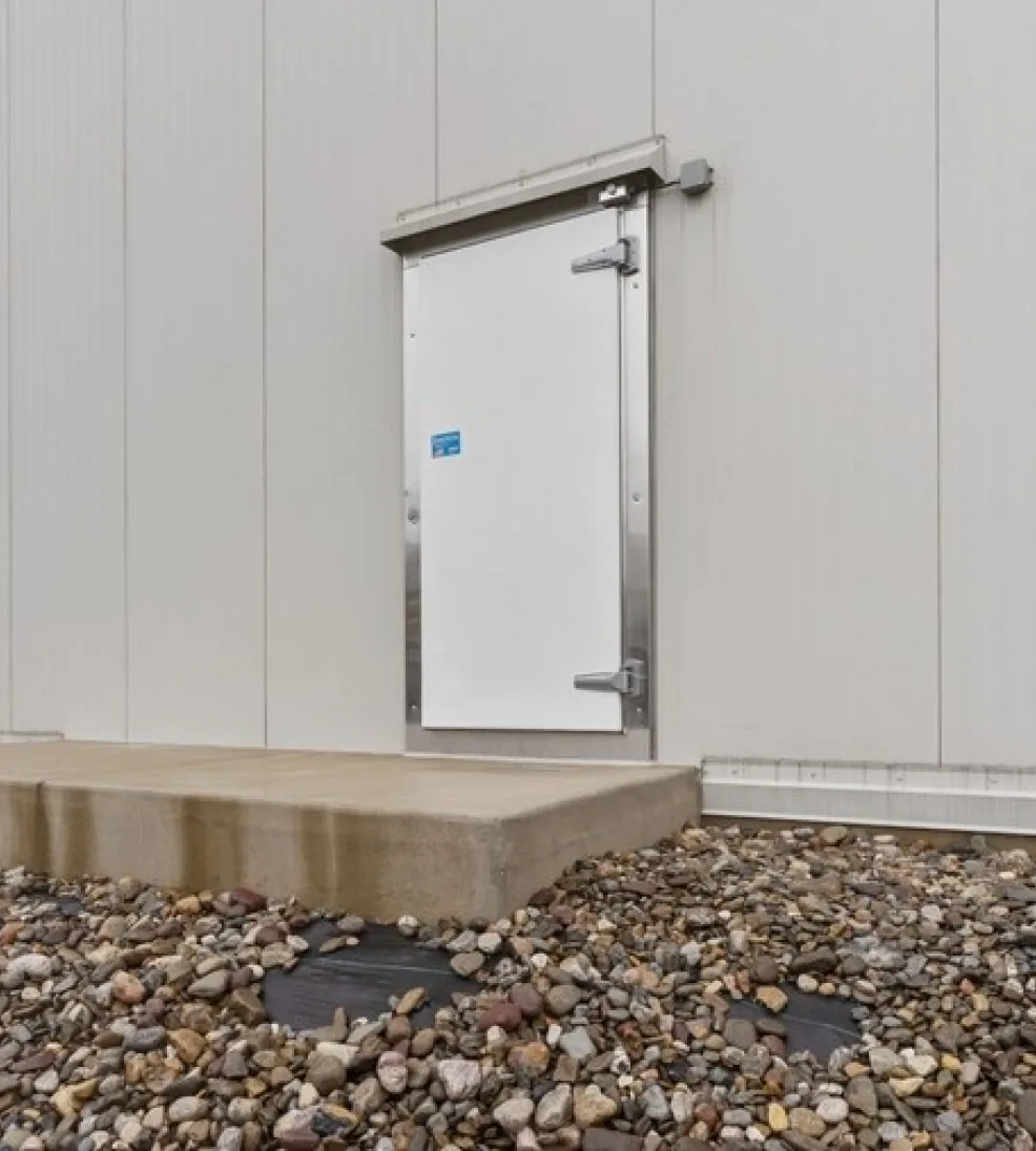 White Jamolite II fiberglass swing door under a hood in an insulated exterior wall above a concrete step
