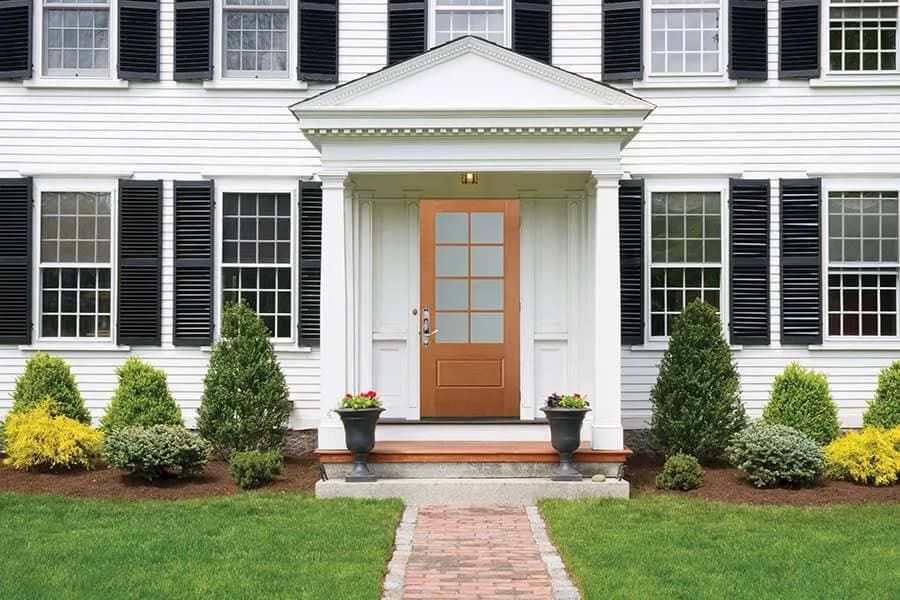 A wood-tone entry door with a divided-lite glass panel on a white colonial house