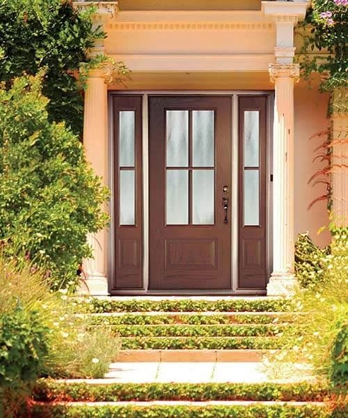 A dark stained entry door with divided-lite glass and two sidelites at the top of brick steps