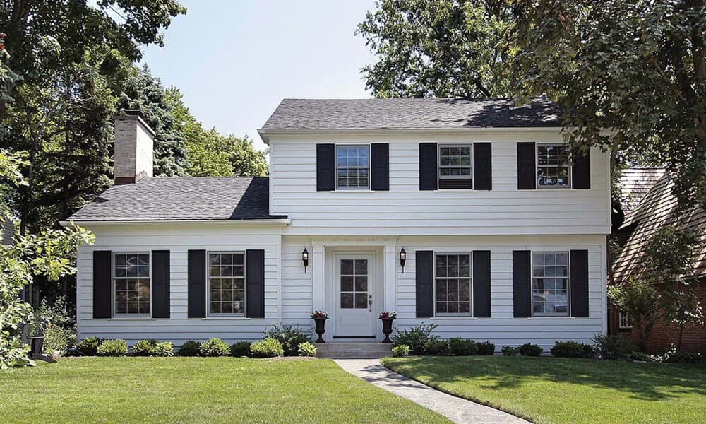 A white entry door with a glass lite on a white colonial house with black shutters
