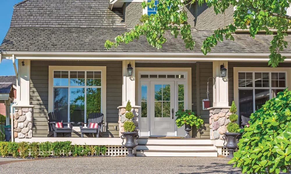 A glass entry door on a gray shingle house with a stone-base porch