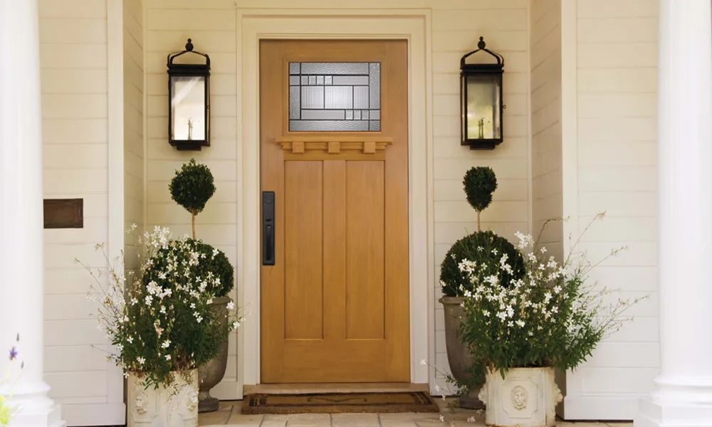 A wood-grain craftsman entry door with a small decorative glass lite between two lanterns