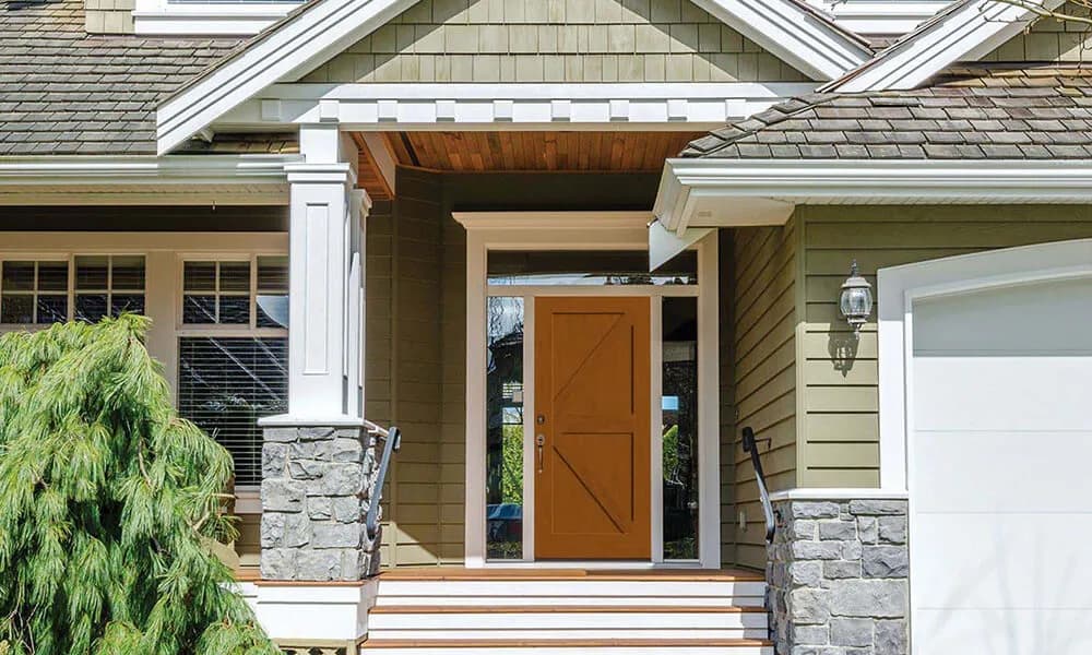 A stained fir-grain entry door with a cross-brace pattern on a craftsman porch