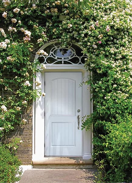 A white arched-panel entry door under a rose-covered arch