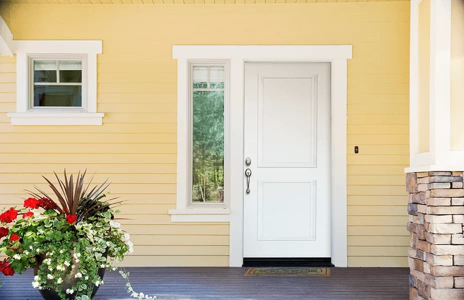 A white two-panel entry door with a sidelite on a yellow house