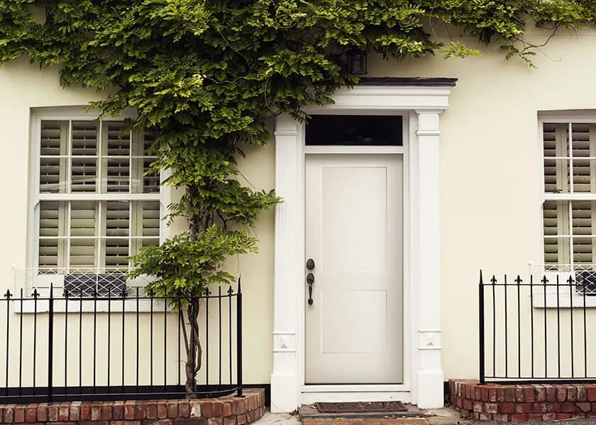 A white panel door under a transom in a cream house with iron railings