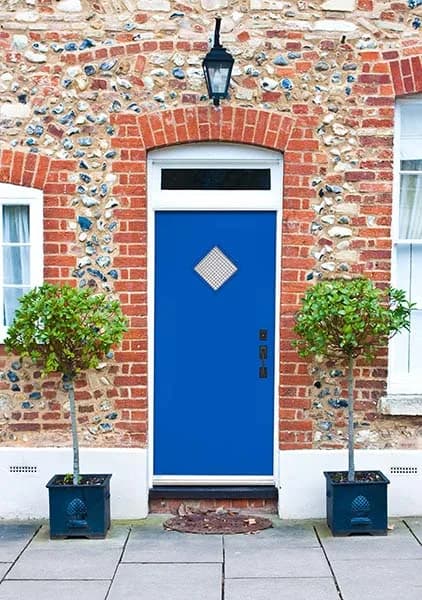 A blue modern entry door with a diamond lite in a brick house