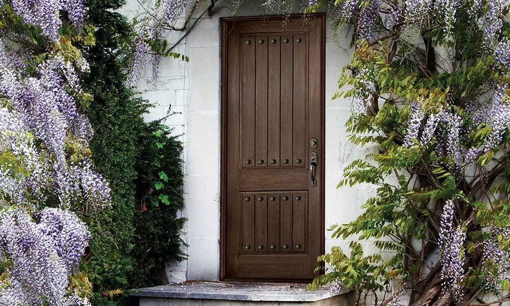 A dark stained plank-style panel entry door framed by wisteria