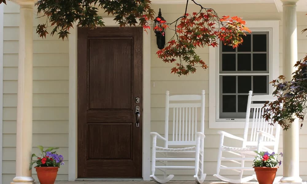 A dark stained panel entry door on a white porch with rocking chairs