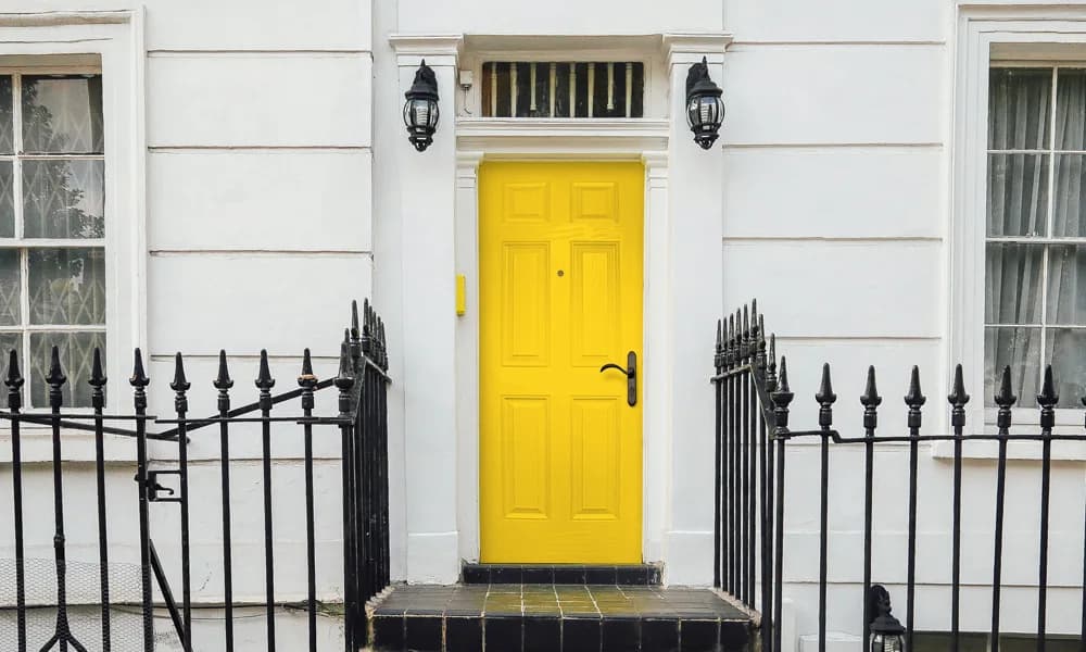 A yellow painted entry door behind a black iron gate
