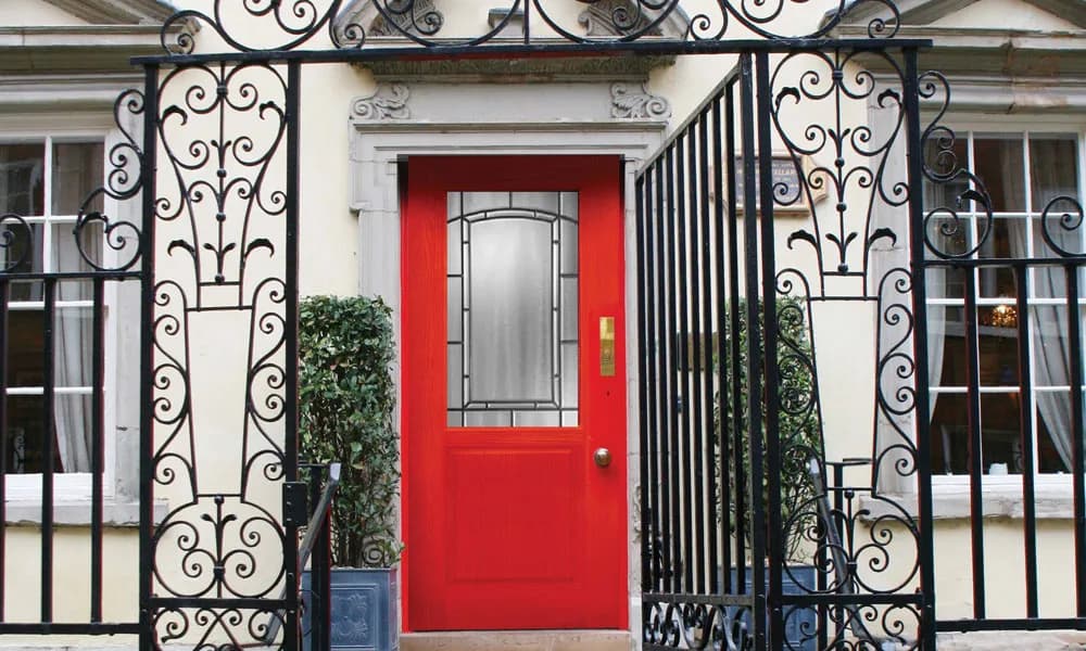 A red painted entry door with decorative glass behind an iron gate