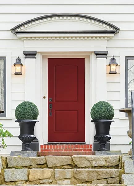A red painted panel entry door between stone planters